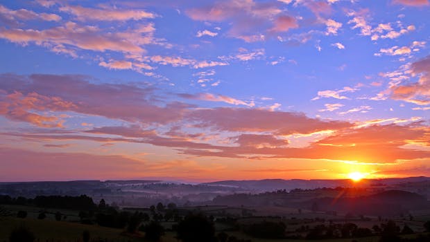 Stunning sunrise over rolling hills with colorful clouds and a vivid skyscape.